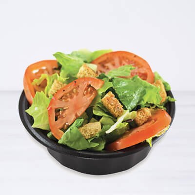 Salade dans un contenant noir, avec laitue, tomates, oignons, croutons et sauce ranch, sur fond blanc